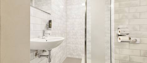 A modern bathroom with a white sink, mirror, and glass shower enclosure.