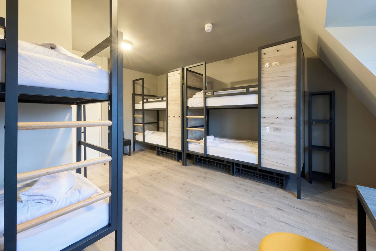 A dormitory room with bunk beds, a small table, and a chair.