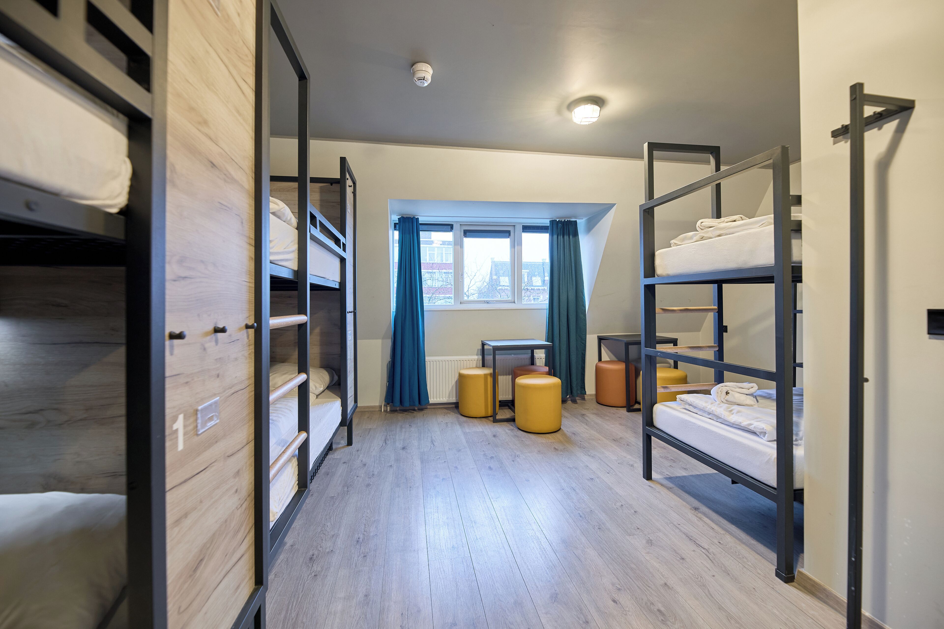 Ein Schlafsaalzimmer mit Etagenbetten, einem Fenster mit Vorhängen und einer Heizung.