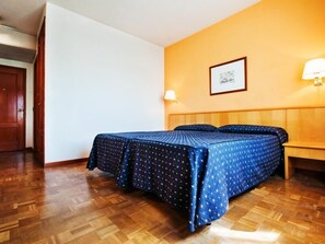 A hotel room with a wooden floor, a bed with a star-patterned bedspread, a wooden headboard, a wall-mounted lamp, and a framed picture on the wall. - Hotel Alcarria (Guadalajara)