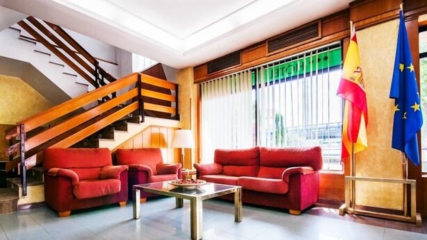 A spacious lobby with a modern staircase, red sofas, a coffee table, and flags. - Hotel Alcarria (Guadalajara)