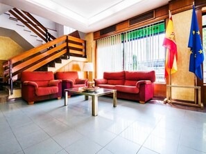 A spacious lobby with a modern staircase, red sofas, a coffee table, and flags. - Hotel Alcarria (Guadalajara)