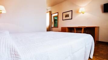 Una habitación de hotel con una cama grande, un escritorio y dos lámparas fijadas a la pared.