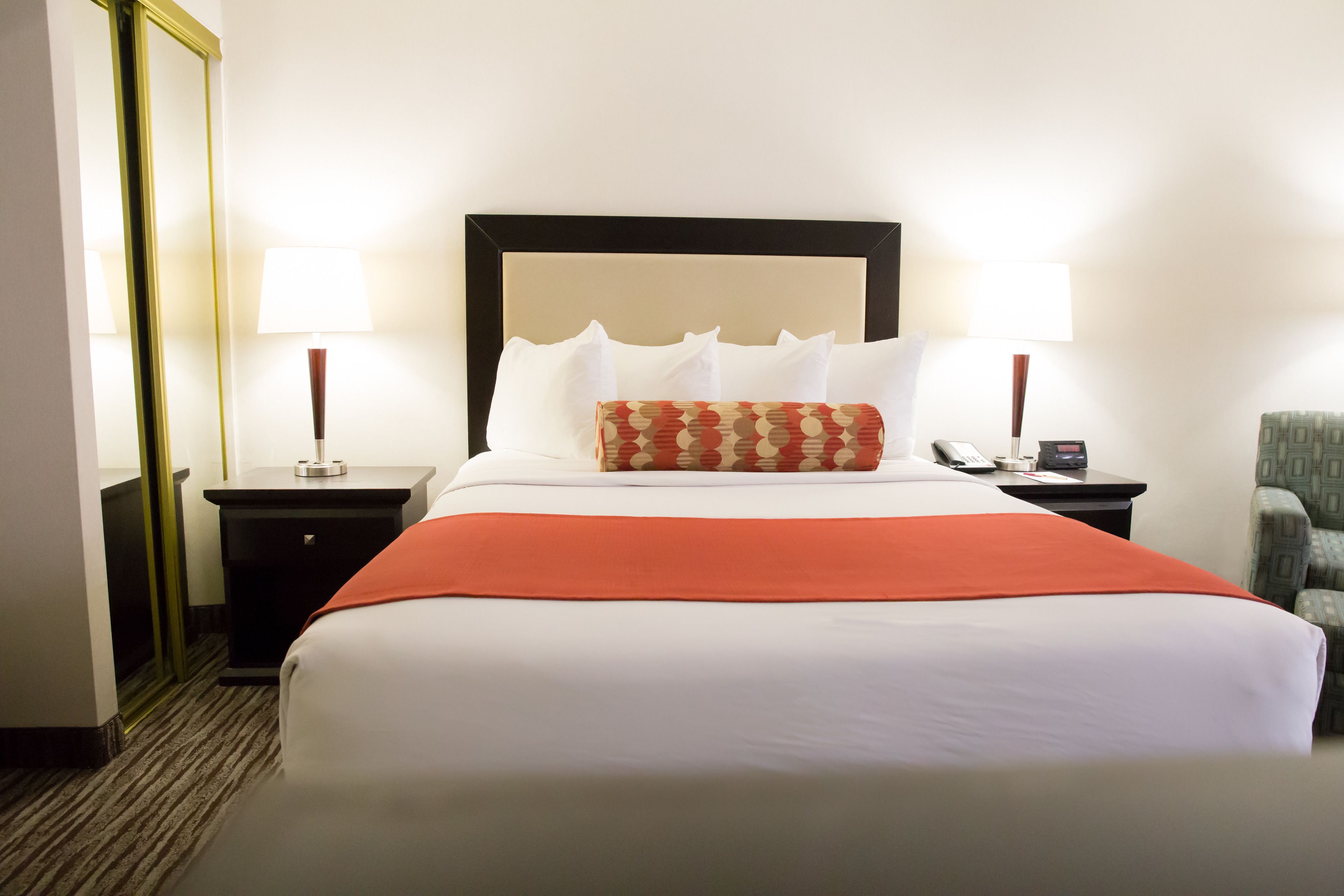 A hotel room with a large bed, two bedside tables, a mirror, a chair, and a lamp.