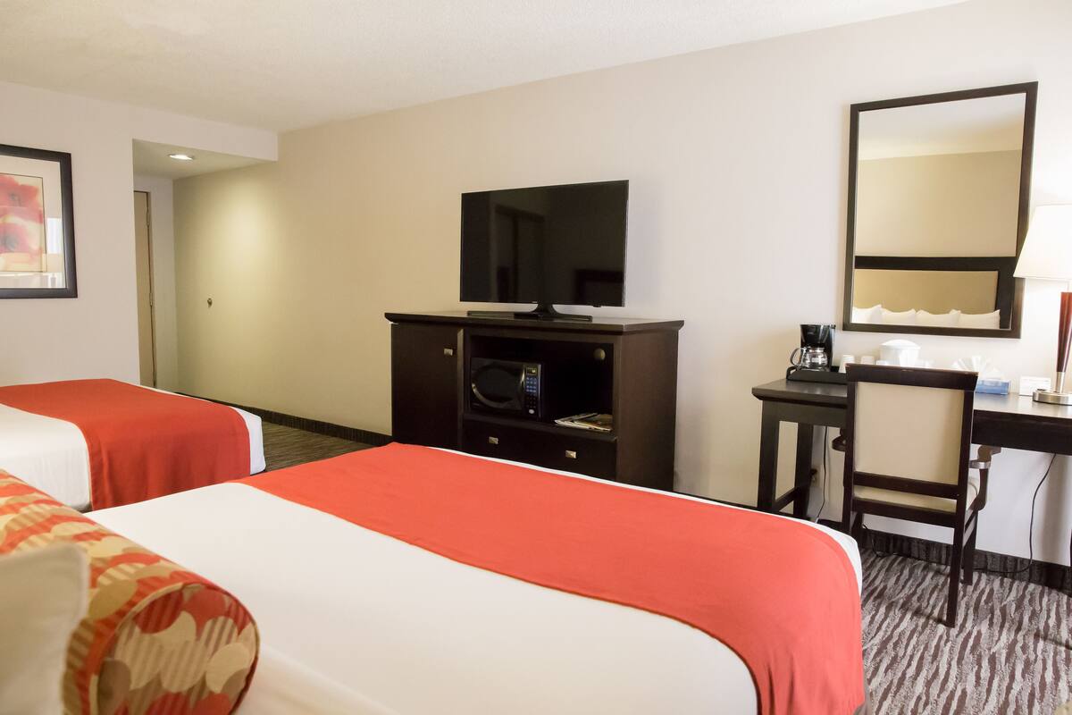 Habitación de hotel con dos camas, un escritorio, una silla, un televisor, un microondas y una cafetera.