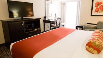 Ein Hotelzimmer mit einem großen Bett, einem Schreibtisch mit Stuhl, einem Fernseher und einem Fenster mit Vorhängen.