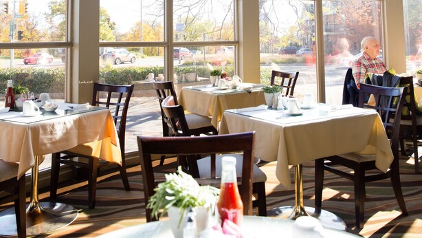 A restaurant with large windows, tables set with white tablecloths, and chairs. - Admiral Inn Hamilton (Hamilton)