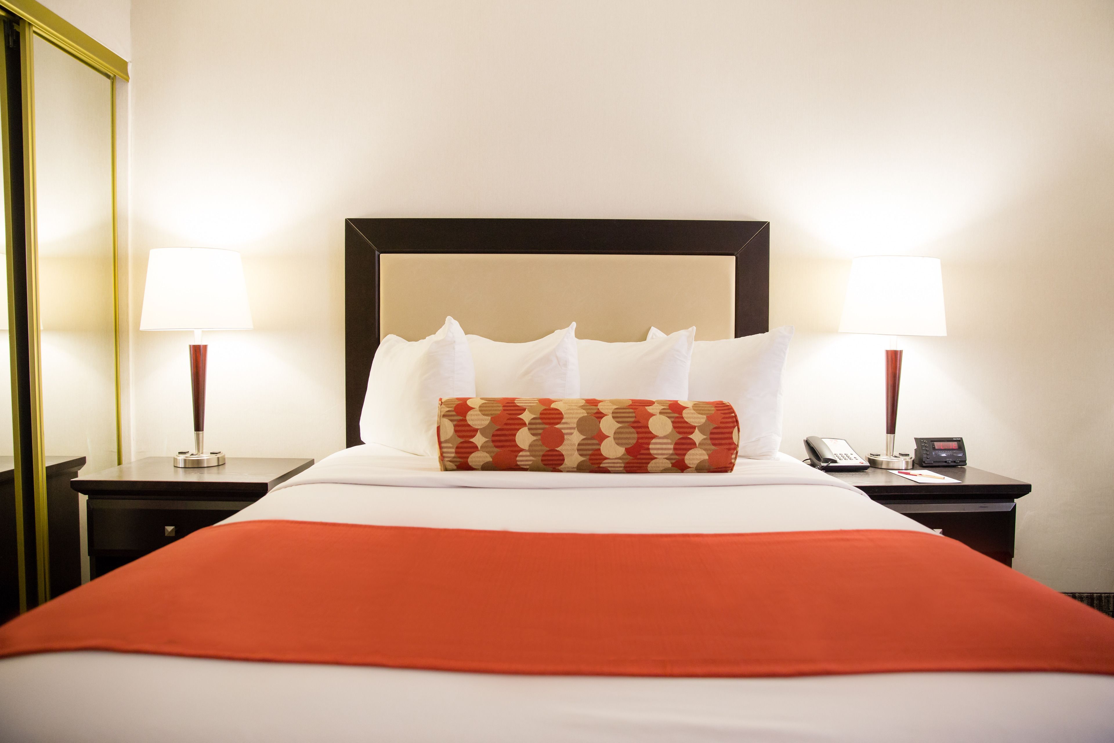 A neatly made bed with a red blanket, two bedside tables with lamps, and a telephone.