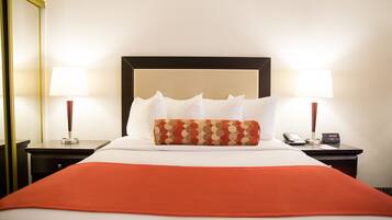 A neatly made bed with a red blanket, two bedside tables with lamps, and a telephone.