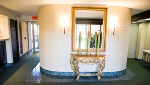 A hallway with a round, cream-colored wall, a gold-framed mirror, and a small table with candles. - Admiral Inn Hamilton (Hamilton)