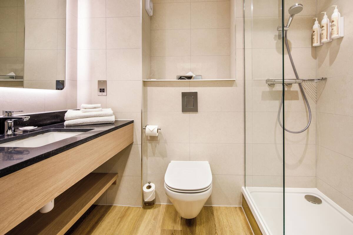Une salle de bain moderne avec un meuble-lavabo en bois, des toilettes blanches et une douche séparée par des parois en verre.