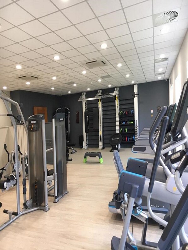 Une salle de sport équipée de divers appareils d’exercice, notamment des tapis de course, des appareils de musculation et un banc.