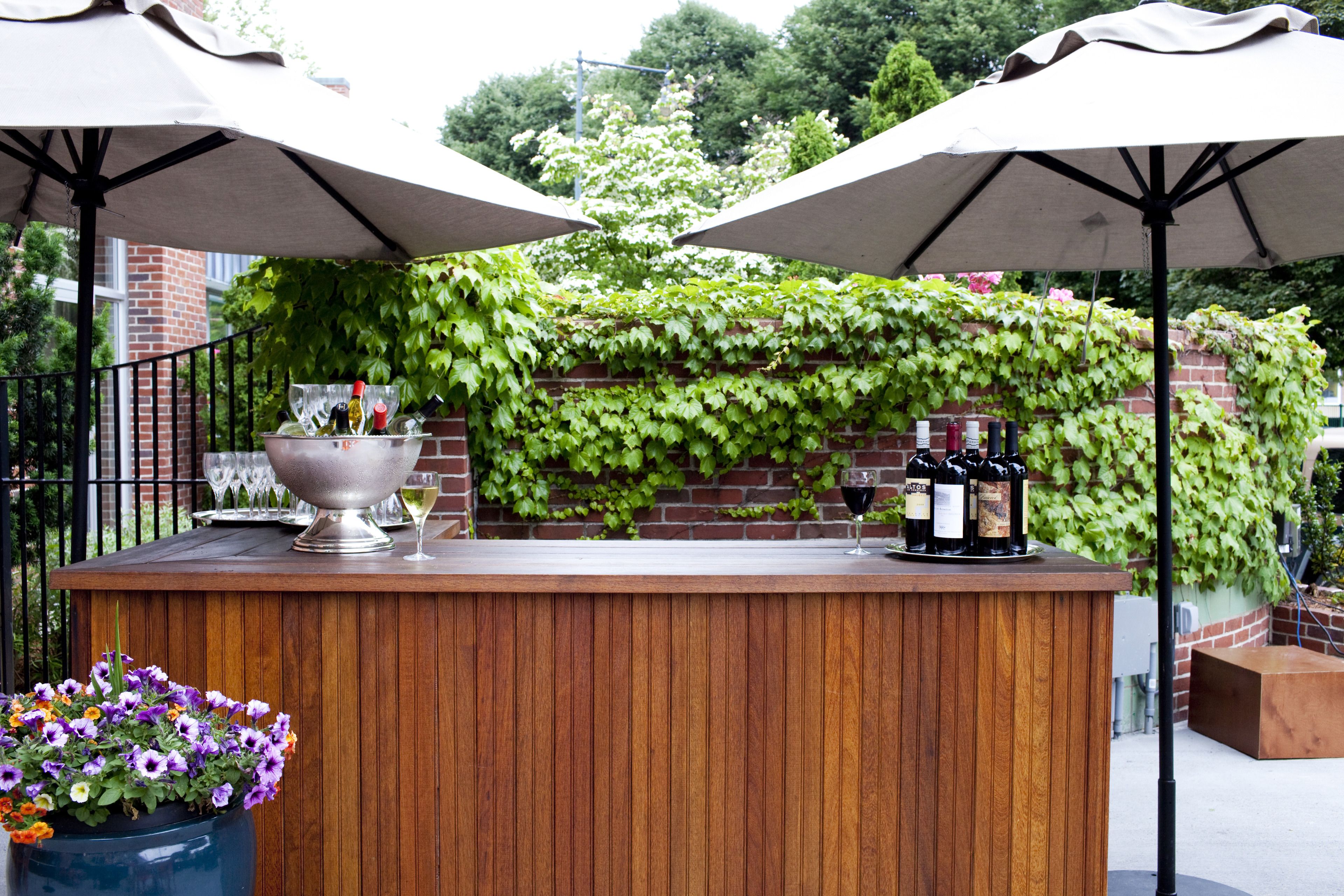 A wooden bar with a metal railing, surrounded by greenery and a brick wall.