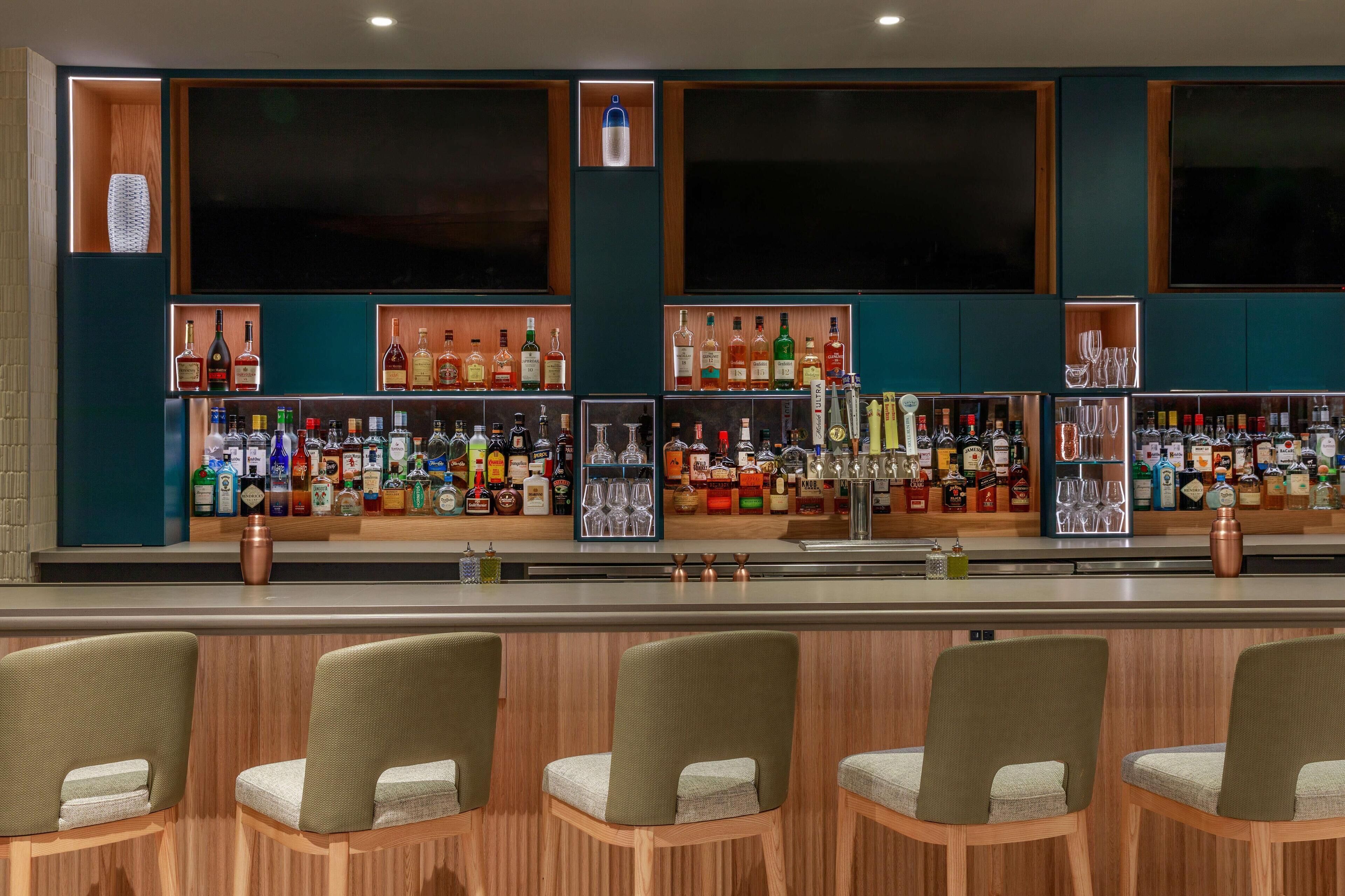 A bar with multiple shelves of liquor bottles, a copper mug, and bar stools.