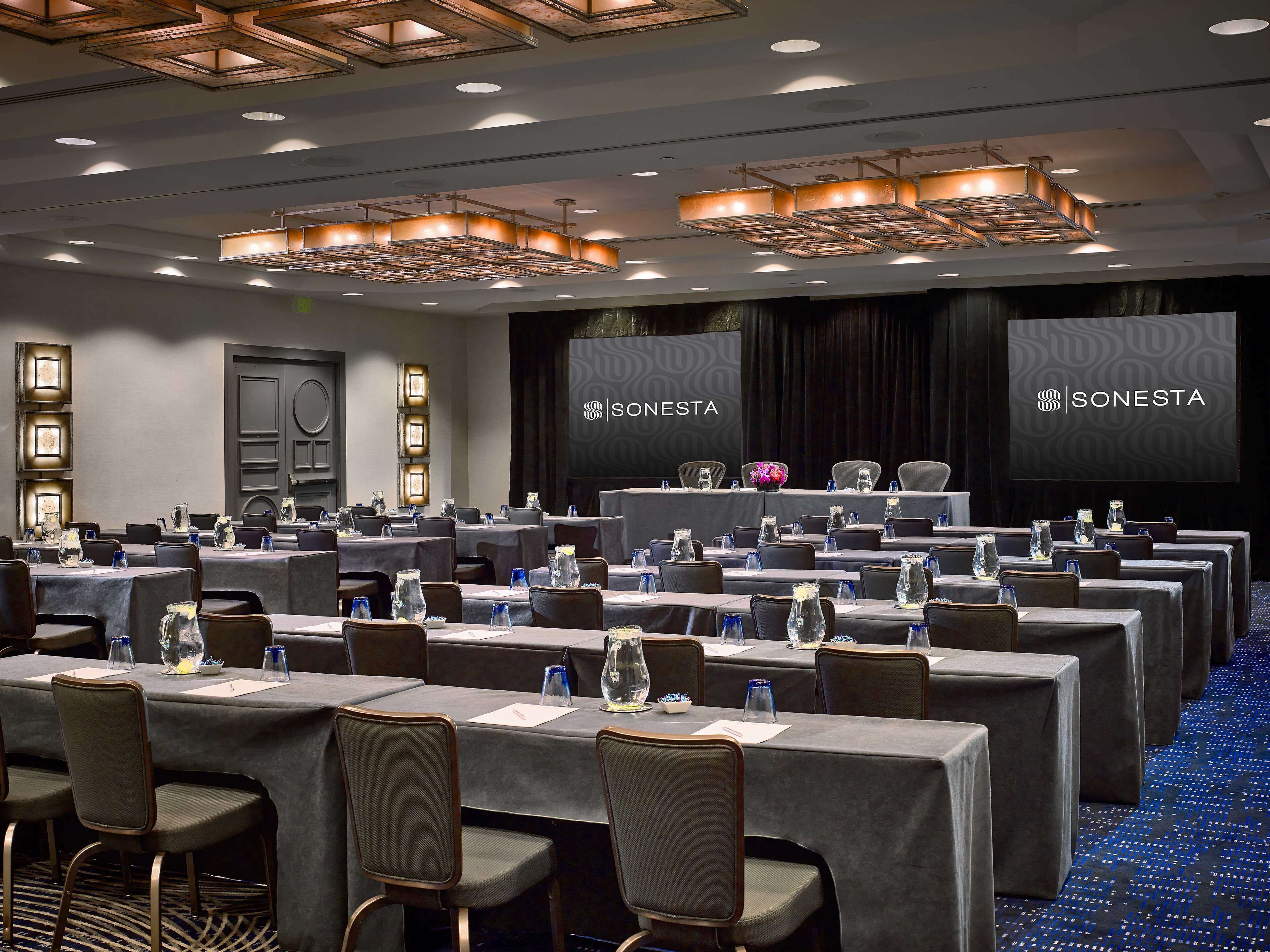 A conference room with multiple tables, chairs, and a stage with a podium.