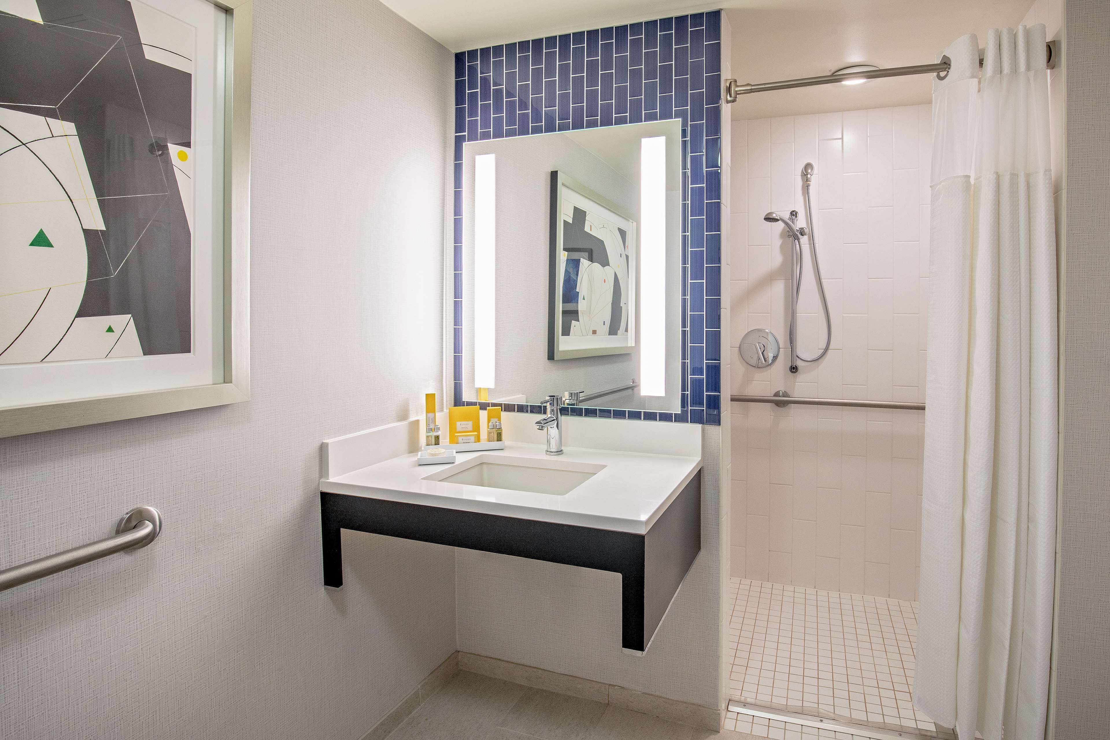 Un bagno con lavandino, specchio, doccia e portasciugamani.
