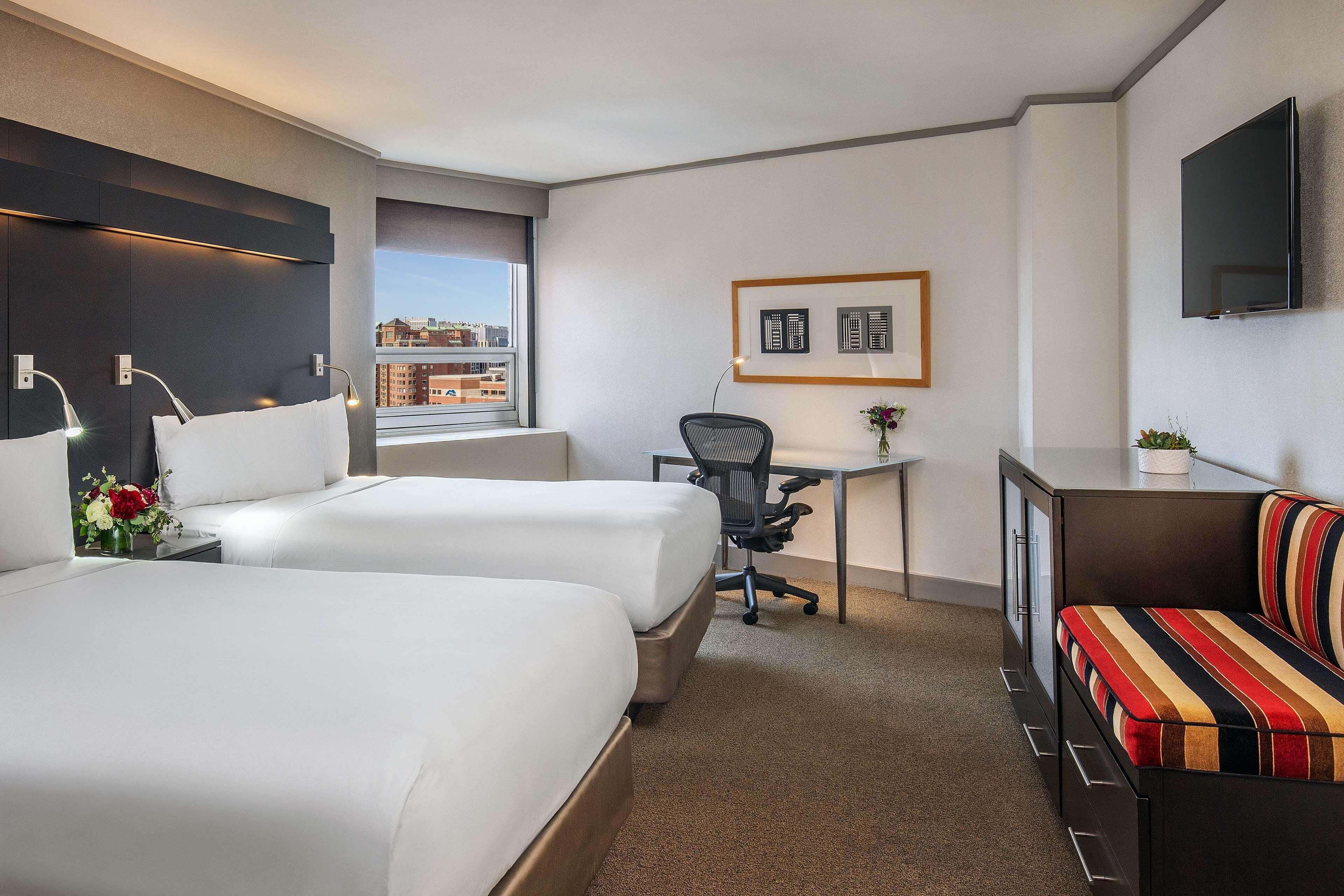 A hotel room with two beds, a desk, a chair, a TV, and a sofa.