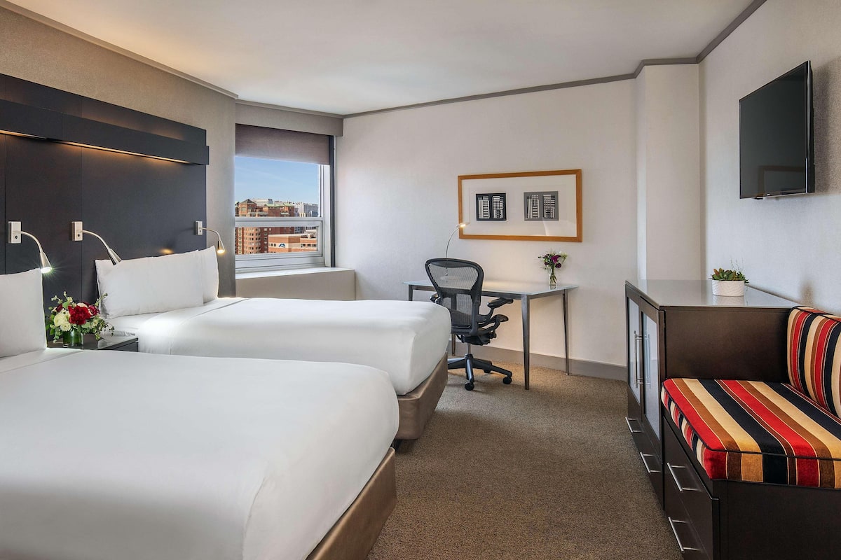 A hotel room with two beds, a desk, a chair, a TV, and a sofa.