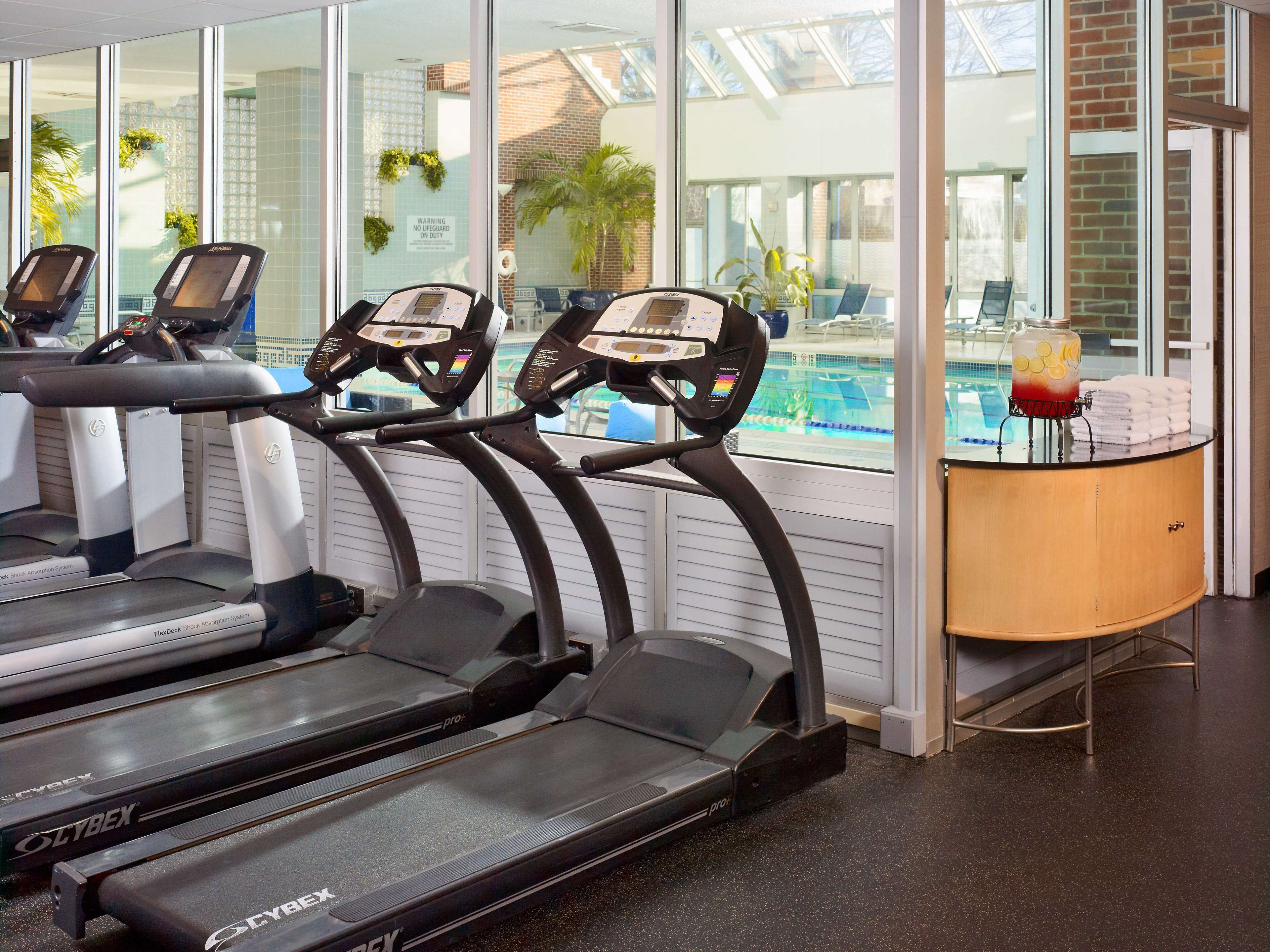 Un gimnasio con cintas de correr, una piscina y un dispensador de agua.
