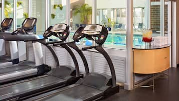 Un gimnasio con cintas de correr, una piscina y un dispensador de agua.