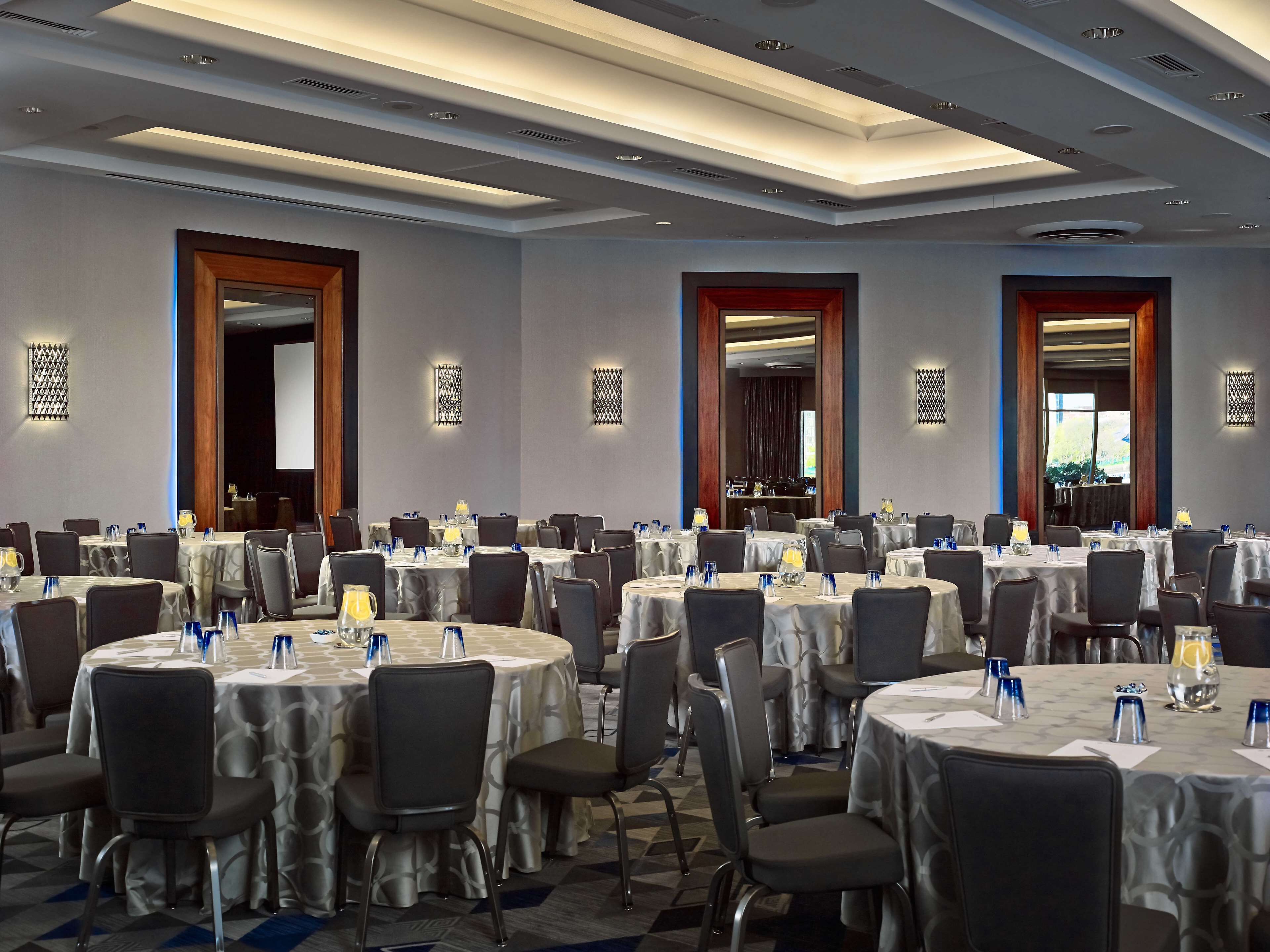 A conference room with multiple round tables, chairs, and tables set with water glasses and pitchers.