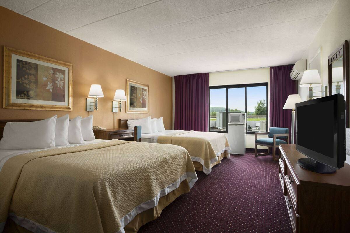Habitación de hotel con dos camas, un escritorio, televisor y ventana con vistas.