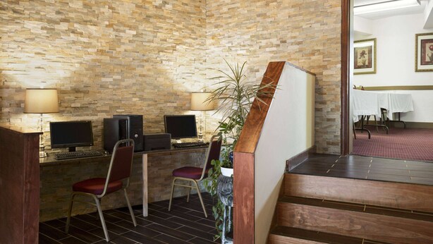 Una habitación con pared de piedra, dos escritorios con computadoras, dos sillas, una planta y una escalera.