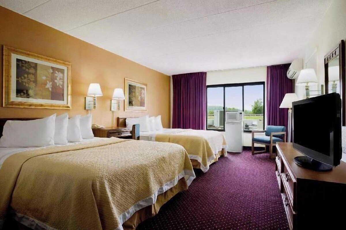 Habitación de hotel con dos camas, televisión, escritorio y ventana con cortinas.
