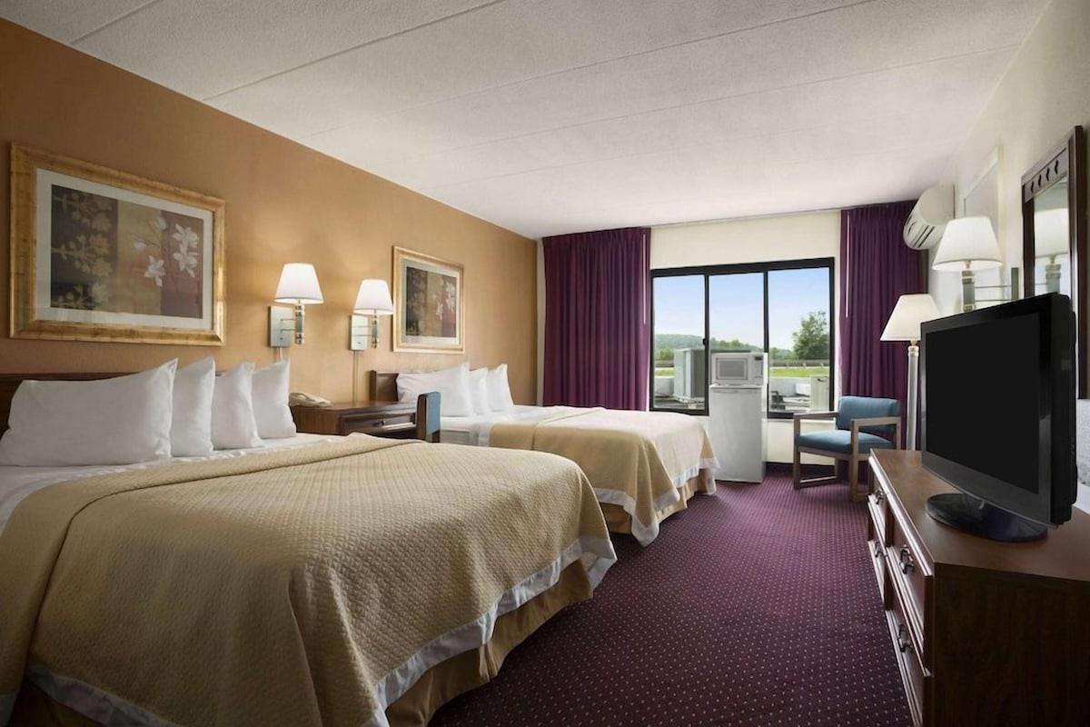 A hotel room with two beds, a television, a desk with a chair, and a window with a view.
