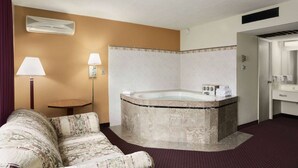Una habitación de hotel con una bañera grande, un sofá, una mesita y una lámpara.