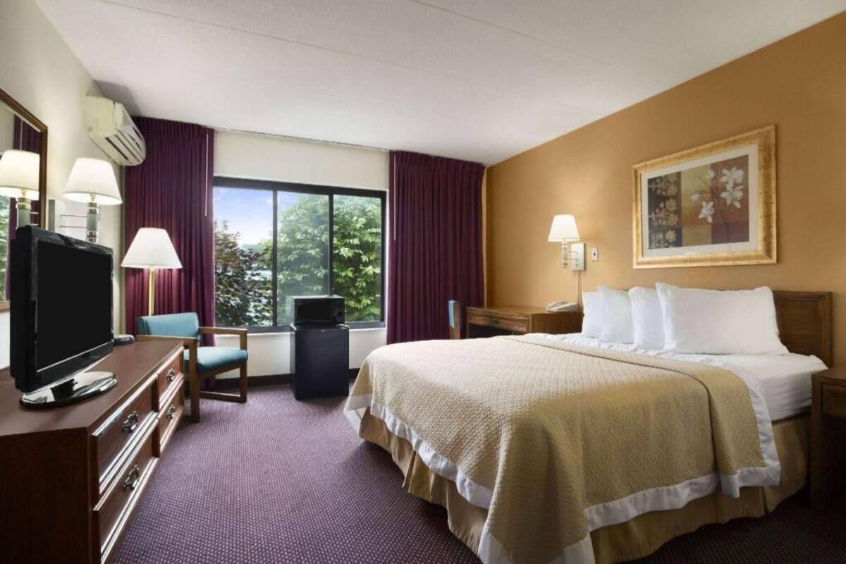 A hotel room with a bed, a TV, a desk, and a window with curtains.