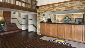 Zona de recepción con un mostrador de madera, una pared de piedra y una escalera que sube a un nivel superior.