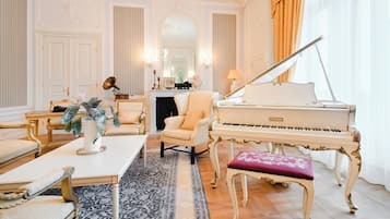 Una sala sontuosa con un pianoforte a coda, arredi eleganti e uno specchio che riflette l'ambiente.