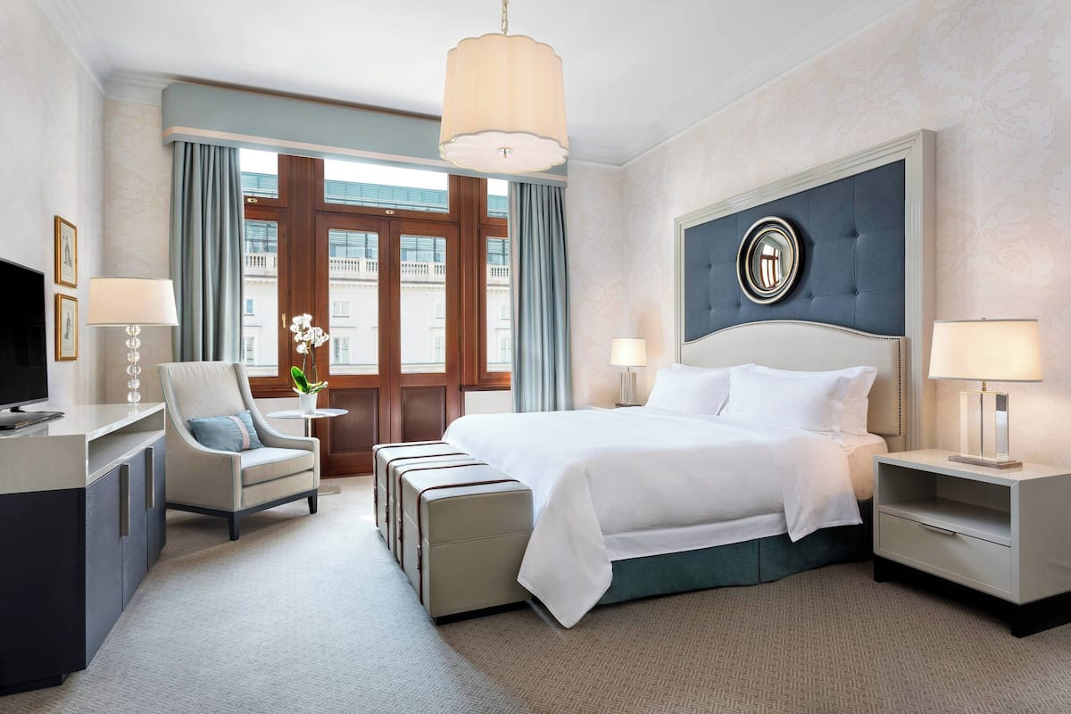 A hotel room with a bed, a desk, a chair, a nightstand, and a window with curtains.