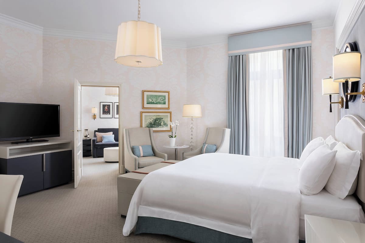 A hotel room with a large bed, a TV, a desk with a chair, and a small table with two chairs.