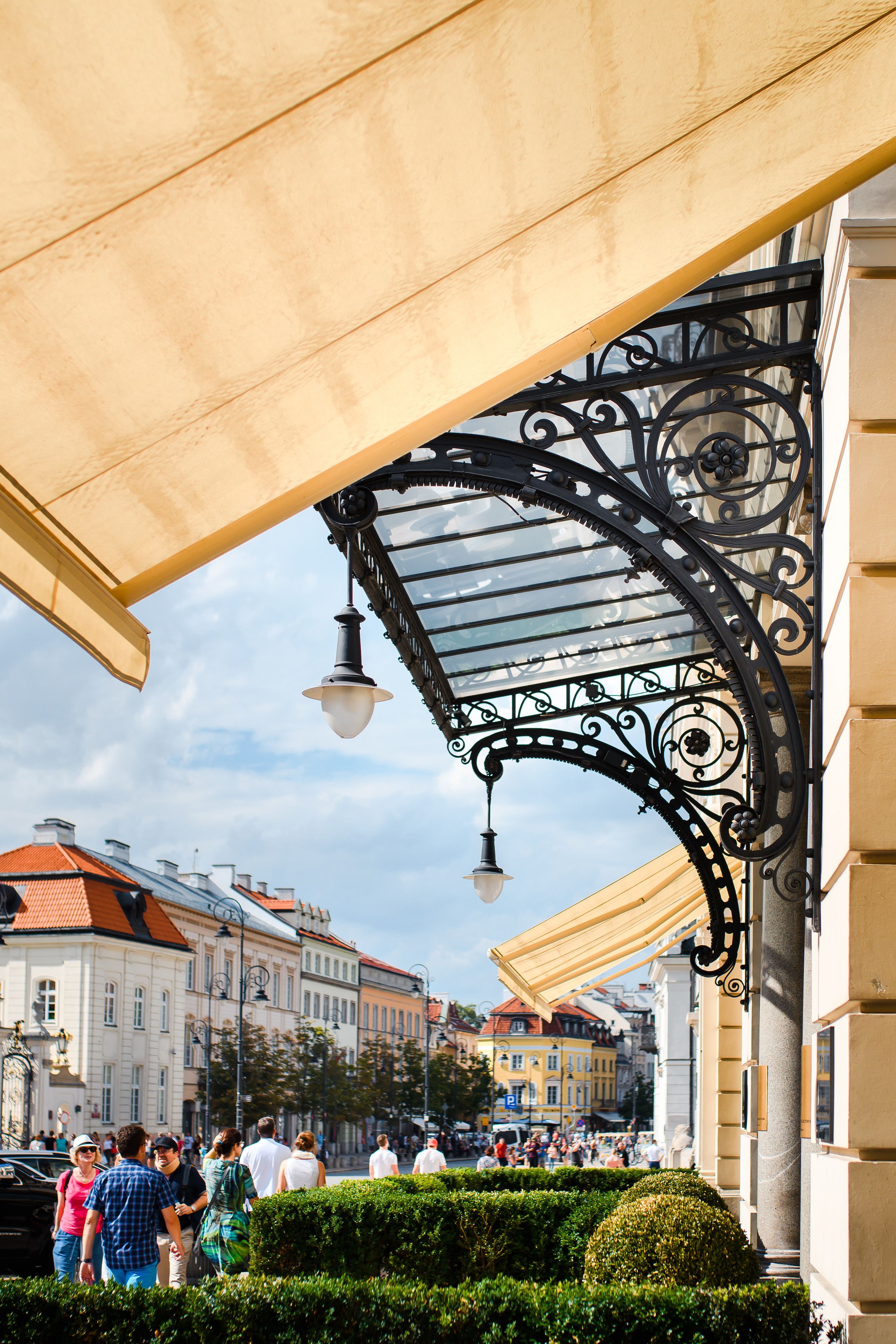 A covered outdoor area with a metal canopy, a street with pedestrians, and buildings in the background.