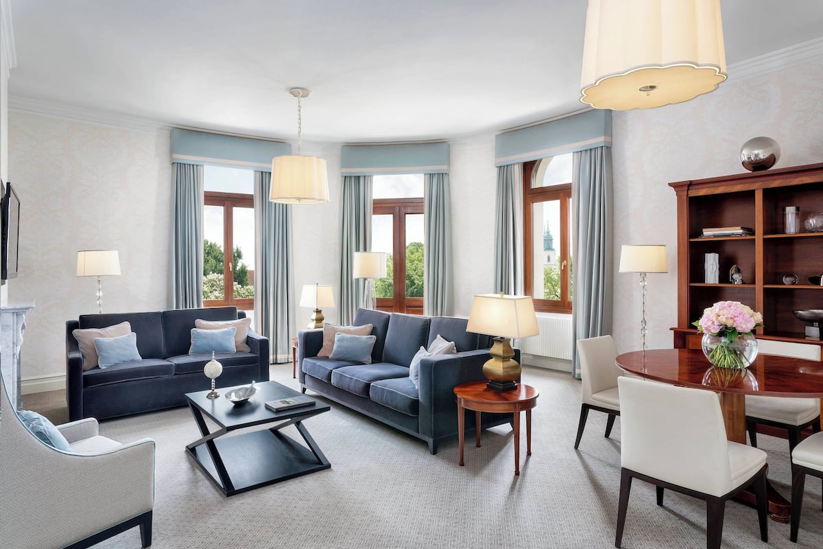 A spacious living room with a dark blue sofa, a coffee table, and a dining table with chairs. There are two lamps on the coffee table and a chandelier above the dining table.