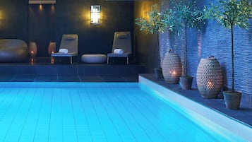 Area piscina interna moderna con pavimento illuminato di blu, sedie a sdraio e fioriere decorative.