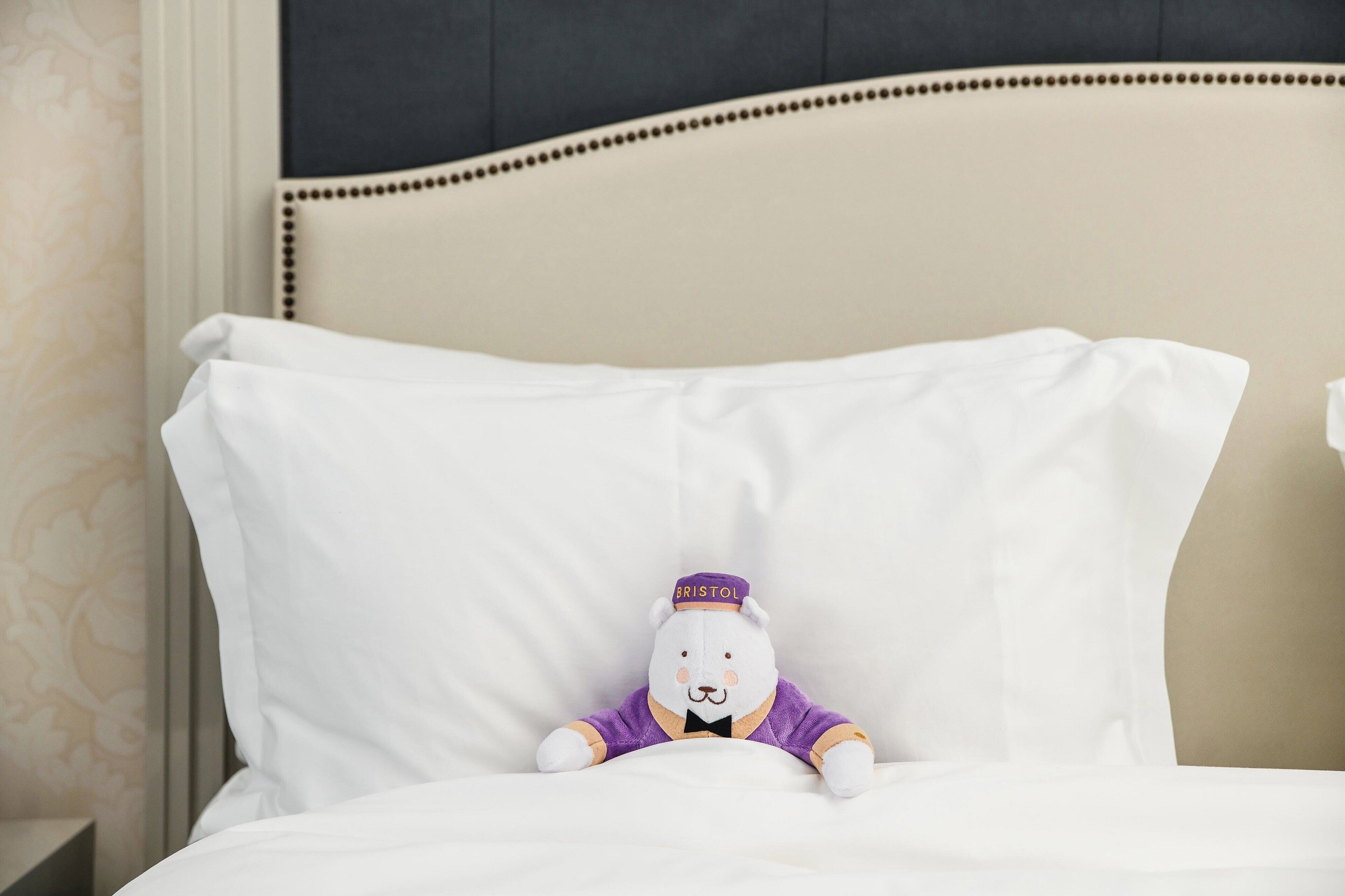 Een zacht knuffeldiertje op een wit kussen in een hotelkamer.