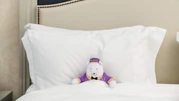 Een zacht knuffeldiertje op een wit kussen in een hotelkamer.