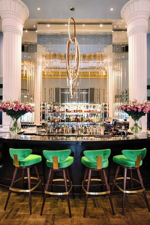 A bar area with a bar counter, green bar stools, and a mirrored wall reflecting the bar.