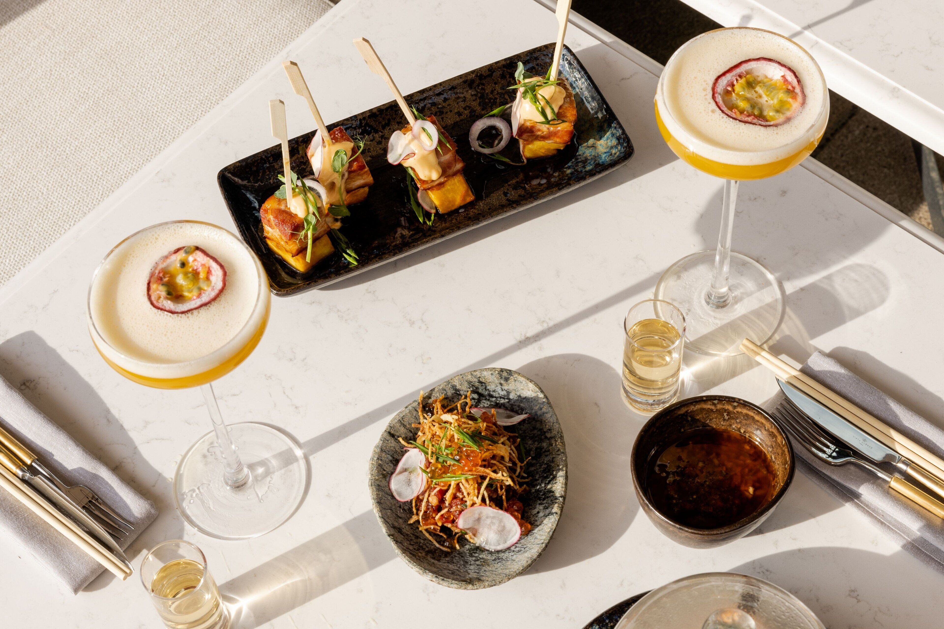 A dining table with a variety of dishes, including skewered appetizers, a bowl of salad, and a glass of wine.