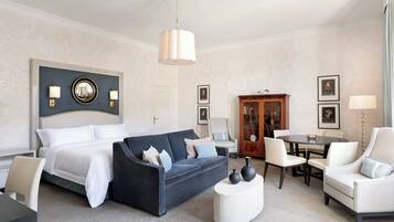A hotel room with a bed, a dark sofa, a white armchair, a round coffee table, and a wooden cabinet.