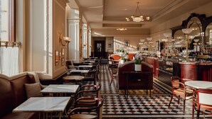 Un'ampia hall d'albergo con pavimento a scacchi, diverse zone relax e un bar con una vasta scelta di prodotti esposti.
