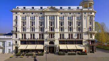 Un grande edificio storico con un ingresso centrale, numerosi balconi e una zona salotto esterna coperta.