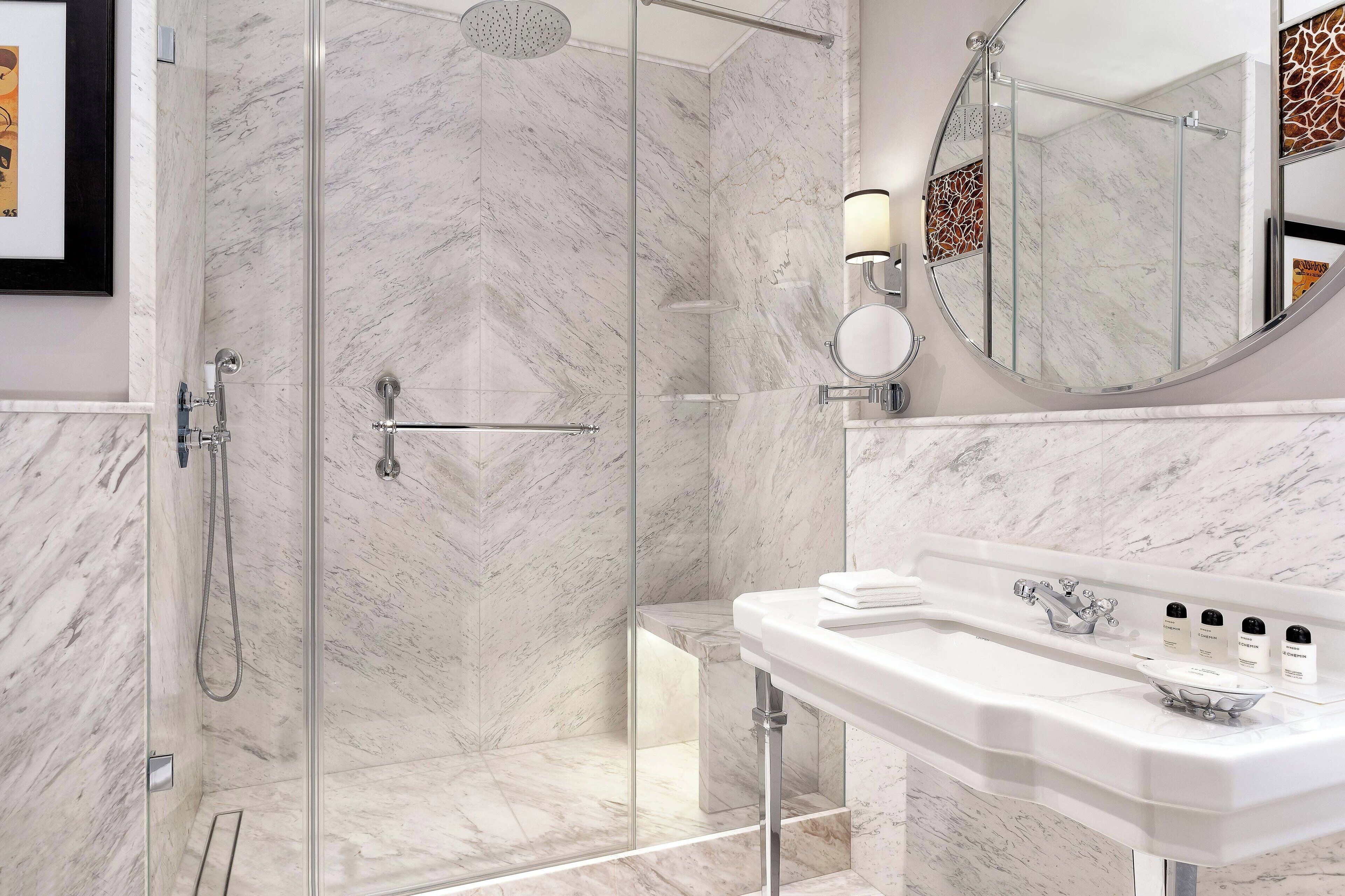 Un baño moderno con ducha de vidrio, un lavamanos blanco con encimera de mármol y un espejo grande con marco decorativo.