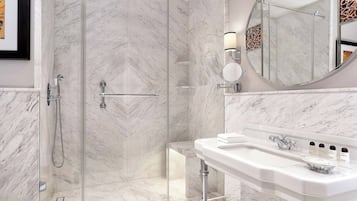 Un baño moderno con ducha de vidrio, un lavamanos blanco con encimera de mármol y un espejo grande con marco decorativo.