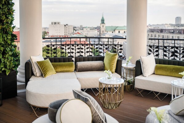 A balcony with a sectional sofa, a small round table, and potted plants.