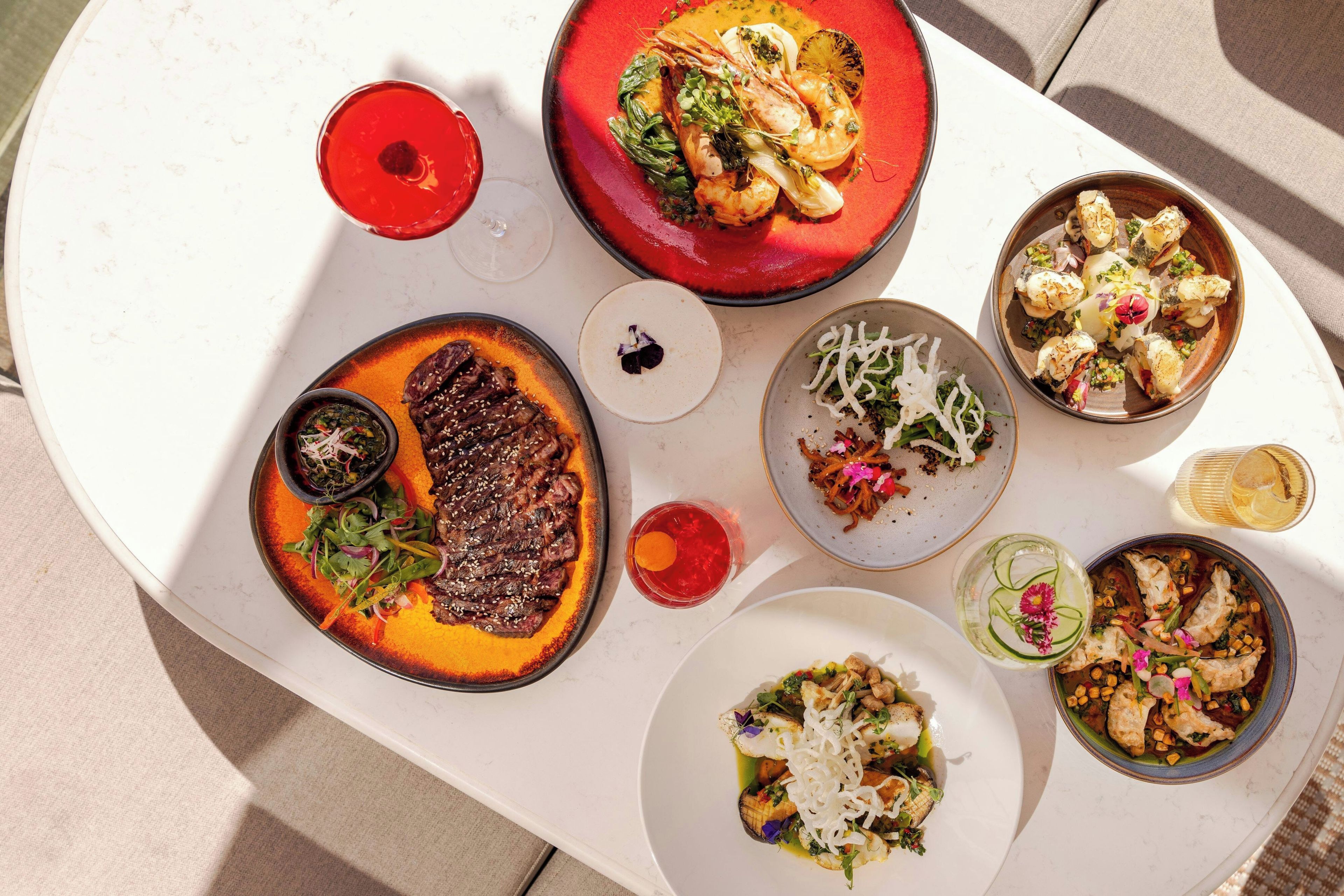 A variety of dishes on a white table, including seafood, steak, and salads.