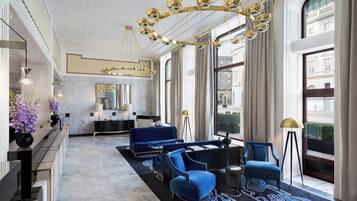A spacious lobby with a modern blue sofa set, a chandelier, and large windows offering views of the city.